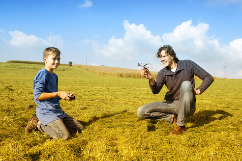 Father and son with remote-controlled helicopter in meadow - MAEF011645