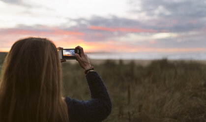 Rückansicht eines Teenagers, der mit seinem Smartphone den Sonnenuntergang fotografiert - MGOF001818