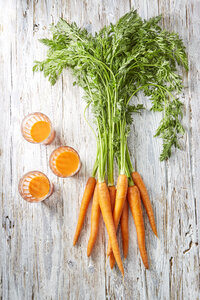 Karotten und drei Gläser Karottensaft auf Holz - KSWF001761