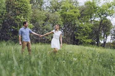 Couple in love holding hands while walking on a meadow - GIOF000985