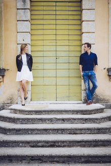 Italy, Verona, couple standing besides wooden door looking at each other - GIOF001006