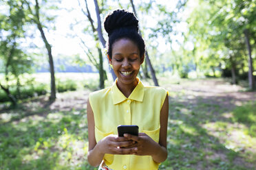 Porträt einer lächelnden jungen Frau in der Natur, die auf ihr Smartphone schaut - GIOF001016