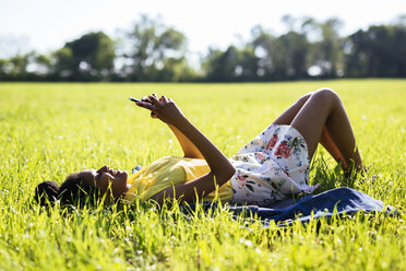 Junge Frau entspannt sich auf einer Wiese und benutzt ihr Smartphone - GIOF001026