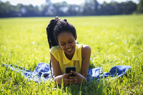 Porträt einer jungen Frau mit Smartphone, die sich auf einer Wiese entspannt - GIOF001028
