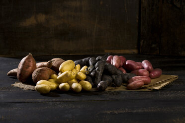 Different sorts of potatoes on brown paper, jute and dark wood - MAEF011671