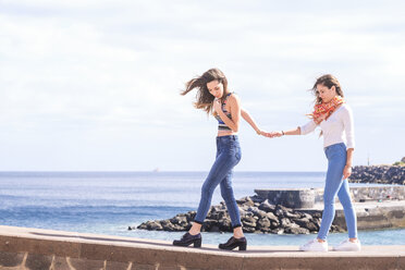 Two friends walking hand in hand on a wall at the ocean - SIPF000468