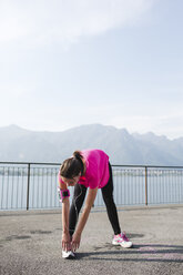 Italien, Lecco, junge Frau streckt sich am See - MRAF000018