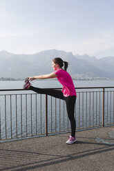 Italien, Lecco, junge Frau streckt sich am See - MRAF000025