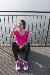 Sportive young woman drinking water after running at lakeshore - MRAF000029