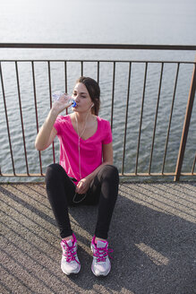 Sportliche junge Frau trinkt Wasser nach einem Lauf am Seeufer - MRAF000029