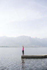 Italien, Lecco, junge Frau streckt sich am See - MRAF000031