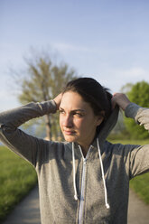 Junge Frau in der Natur beim Aufsetzen der Kapuze ihrer Kapuzenjacke - MRAF000038