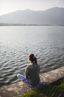 Italien, Lecco, entspannte junge Frau, die am Seeufer sitzt - MRAF000039