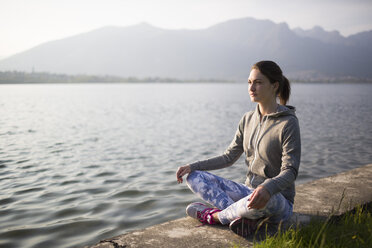 Italy, Lecco, relaxed young woman sitting at the lakeshore - MRAF000040