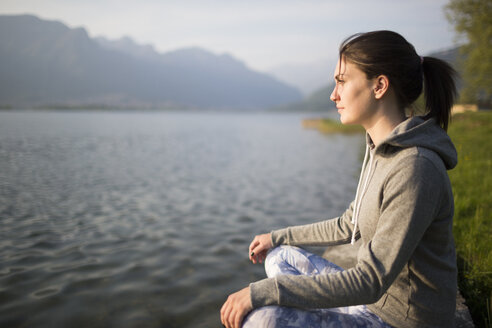 Italien, Lecco, entspannte junge Frau, die am Seeufer sitzt - MRAF000042