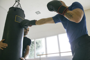 Boxer schlägt auf einen Sandsack, der von einem Trainingspartner gehalten wird - ABZF000483