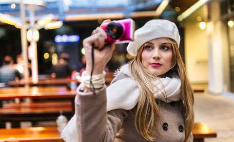 Porträt einer jungen Frau mit Baskenmütze, die ein Selfie mit einer Digitalkamera macht, lizenzfreies Stockfoto