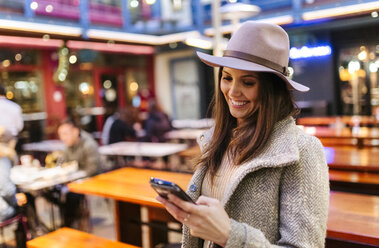 Porträt einer lächelnden jungen Frau, die auf ihr Smartphone schaut - MGOF001828