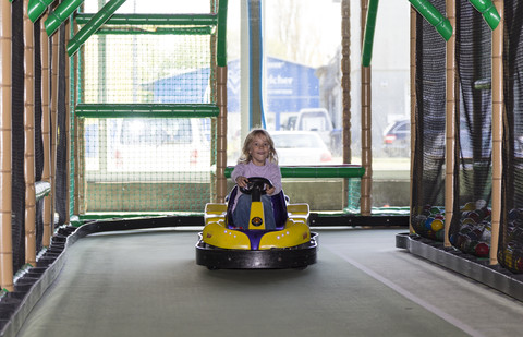 Aufgeregtes kleines Mädchen fährt Autoscooter in einem Indoor-Spielplatz, lizenzfreies Stockfoto