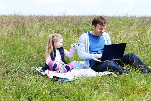 Vater und Tochter sitzen auf der Wiese, Smartphone und Laptop - MAEF011728