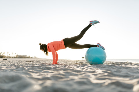 Frau beim Sport mit Gymnastikball früh am Morgen am Strand, lizenzfreies Stockfoto