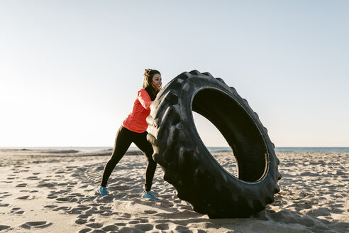 Frau beim Sport mit Traktorreifen früh am Morgen am Strand - JRFF000673