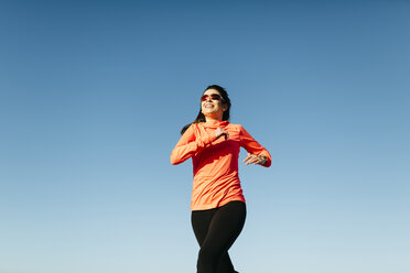 Junge Frau beim Joggen, blauer Himmel - JRFF000678