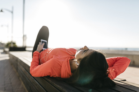 Frau ruht sich aus und benutzt das Telefon nach dem Laufen, lizenzfreies Stockfoto