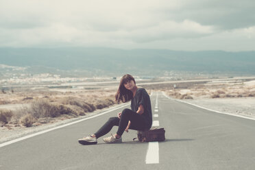 Young woman with suitcase sitting on the road - SIPF000483
