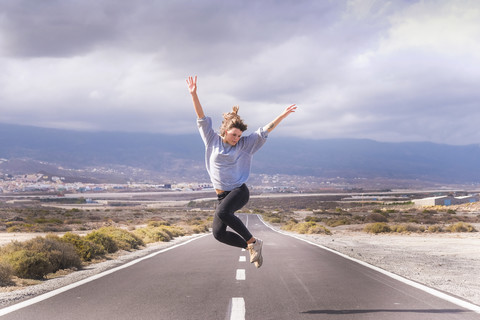 Junge Frau springt vor Freude auf einer Straße, lizenzfreies Stockfoto