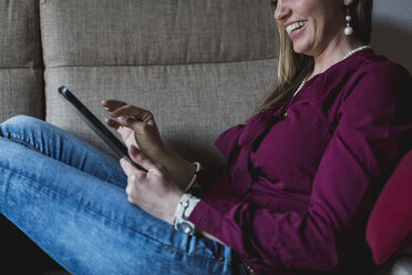 Young woman sitting on couch using digital tablet - MAUF000580