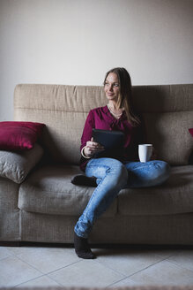 Junge Frau sitzt auf der Couch und benutzt ein digitales Tablet - MAUF000582