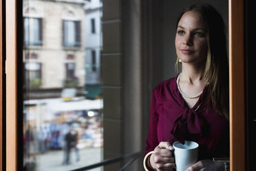 Young woman standing by window, drinking coffee - MAUF000584