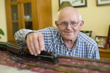 Porträt eines lächelnden älteren Mannes mit seiner Modelleisenbahn - RAEF001158