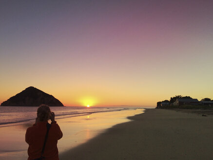 Neuseeland, Nordinsel, East Cape Region, Sonnenaufgang in der Anaura Bay, Frau fotografiert den ersten Sonnenaufgang des Tages - GWF004694