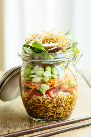 Asian salad in a jar with ramen noodles, red pepper, snow pea pods, carrots, edamame, shiitake mushrooms, salad greens, fried chow mien noodles and dressing stock photo