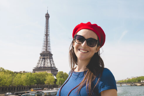 Frankreich, Paris, Porträt einer lächelnden Frau mit Sonnenbrille und roter Baskenmütze vor dem Eiffelturm - GEMF000899