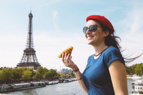 Frankreich, Paris, Frau mit Croissant vor der Seine und dem Eiffelturm stehend - GEMF000902