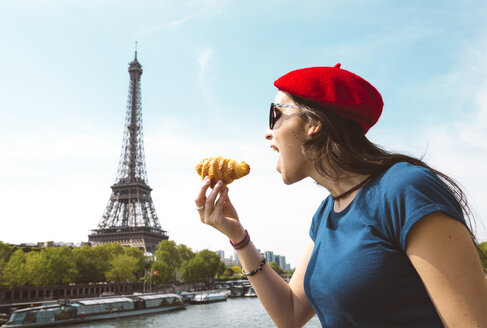 Frankreich, Paris, Frau isst Croissant vor der Seine und dem Eiffelturm - GEMF000903