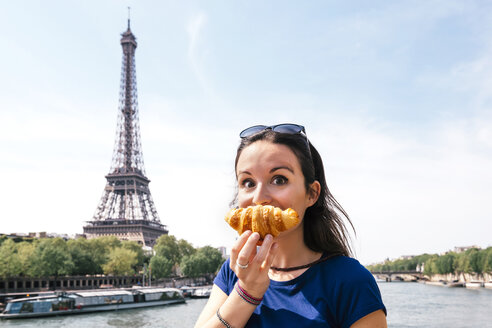 France, Paris, staring woman with croissant in front of Seine river and Eiffel Tower - GEMF000904