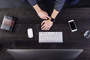 Man working at desk with computer, sychronizing smart watch - HAPF000338