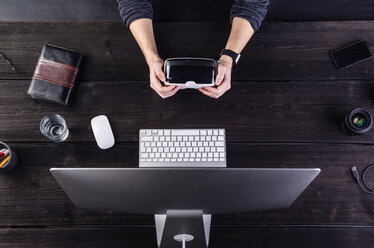 Man sitting at desk holding VR goggles - HAPF000346