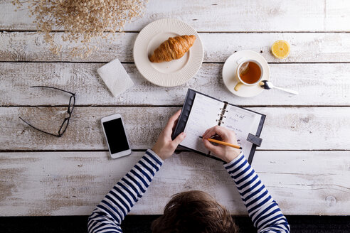 Mann arbeitet mit Smartphone und Organizer beim Frühstück - HAPF000356