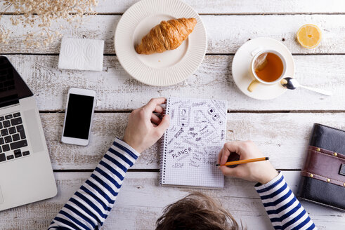 Mann arbeitet am Tisch mit Croissant und Tee und macht sich Notizen - HAPF000358