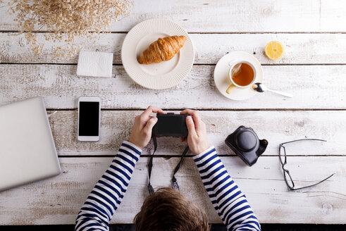 Mann arbeitet an einem Tisch mit Croissant und Tee und schaut in seine Kamera - HAPF000359