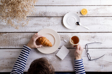 Mann sitzt am Tisch und trinkt Tee und isst ein Croissant - HAPF000360