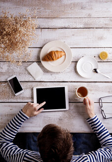 Mann arbeitet am Tisch mit Croissant und Tee, mit digitalem Tablet - HAPF000361