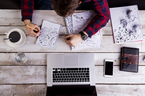 Mann arbeitet am Schreibtisch mit Laptop und macht Notizen, lizenzfreies Stockfoto