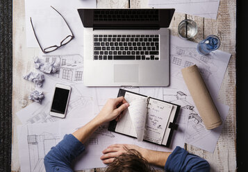 Architektin arbeitet am Schreibtisch mit Laptop und schaut auf einen persönlichen Organizer - HAPF000379