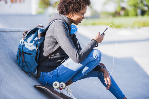 Junge Frau mit Kopfhörern, Mobiltelefon und Skateboard - UUF007241